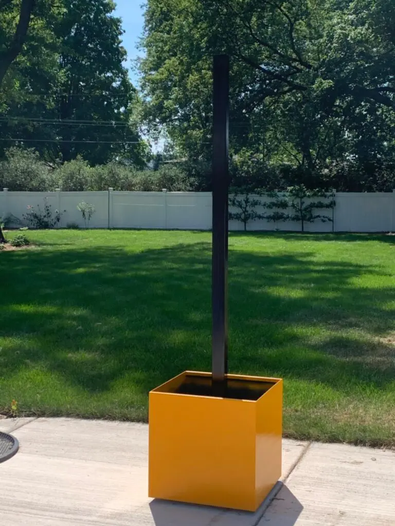 A yellow aluminum planter with a leg for a gazebo inside of it.